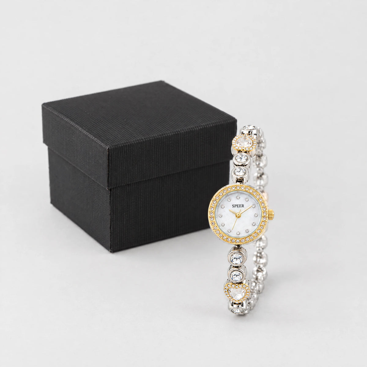 Two-tone LOLA Heart Bracelet Watch standing in front of a small black textured gift box
