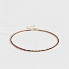 Gold Tessa Birthstone Tennis Necklace with garnet red January birthstone-color crystals on a light grey background