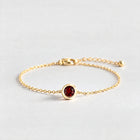 Gold Zara Birthstone Charm Bracelet with garnet red January birthstone-color crystal on a light grey background