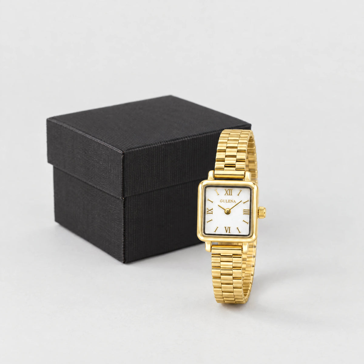 Gold CLARA Square Bracelet Watch standing in front of a small black textured gift box