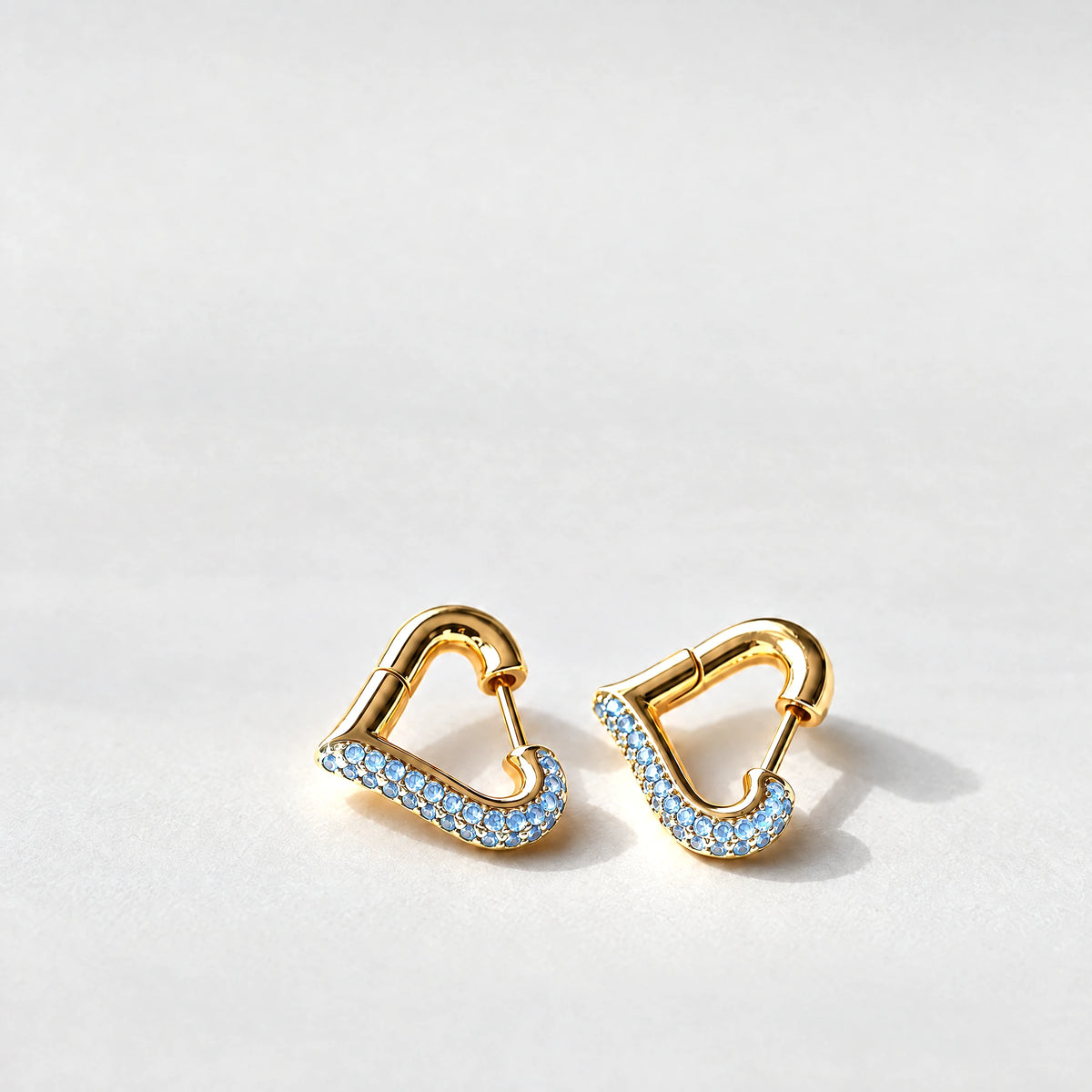 Gold Cora Crystal Heart Hoop Earrings with blue crystals on a light grey background