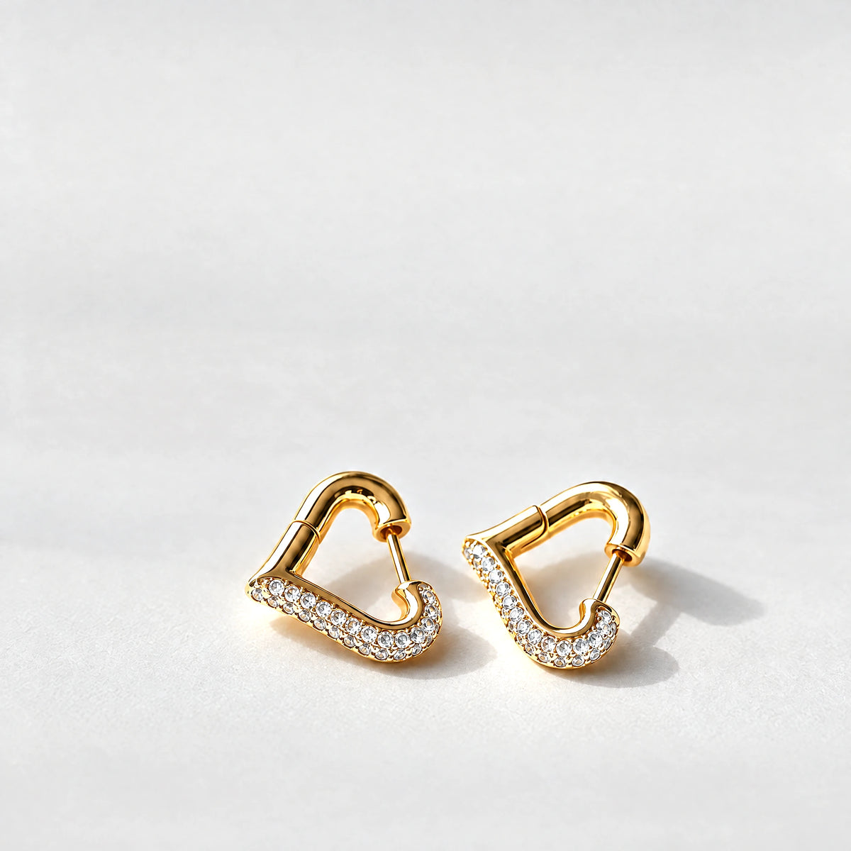 Gold Cora Crystal Heart Hoop Earrings with clear crystals on a light grey background