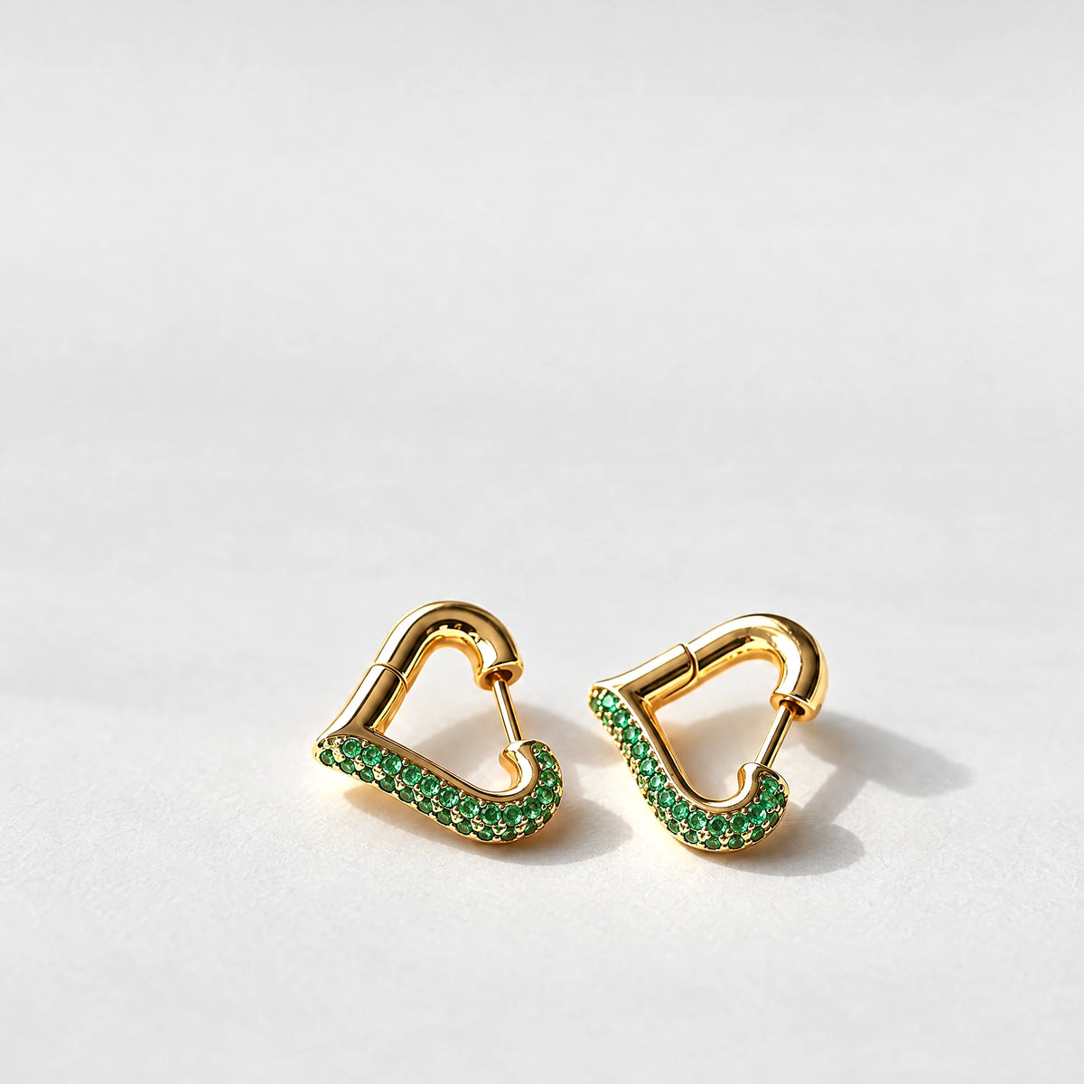 Gold Cora Crystal Heart Hoop Earrings with green crystals on a light grey background