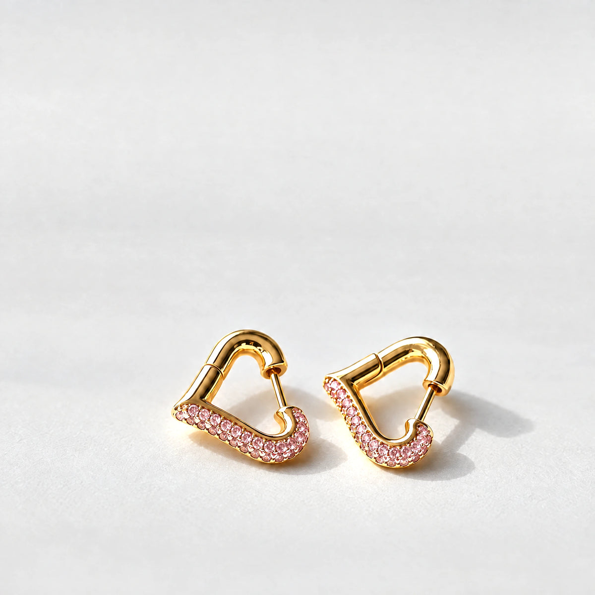 Gold Cora Crystal Heart Hoop Earrings with pink crystals on a light grey background