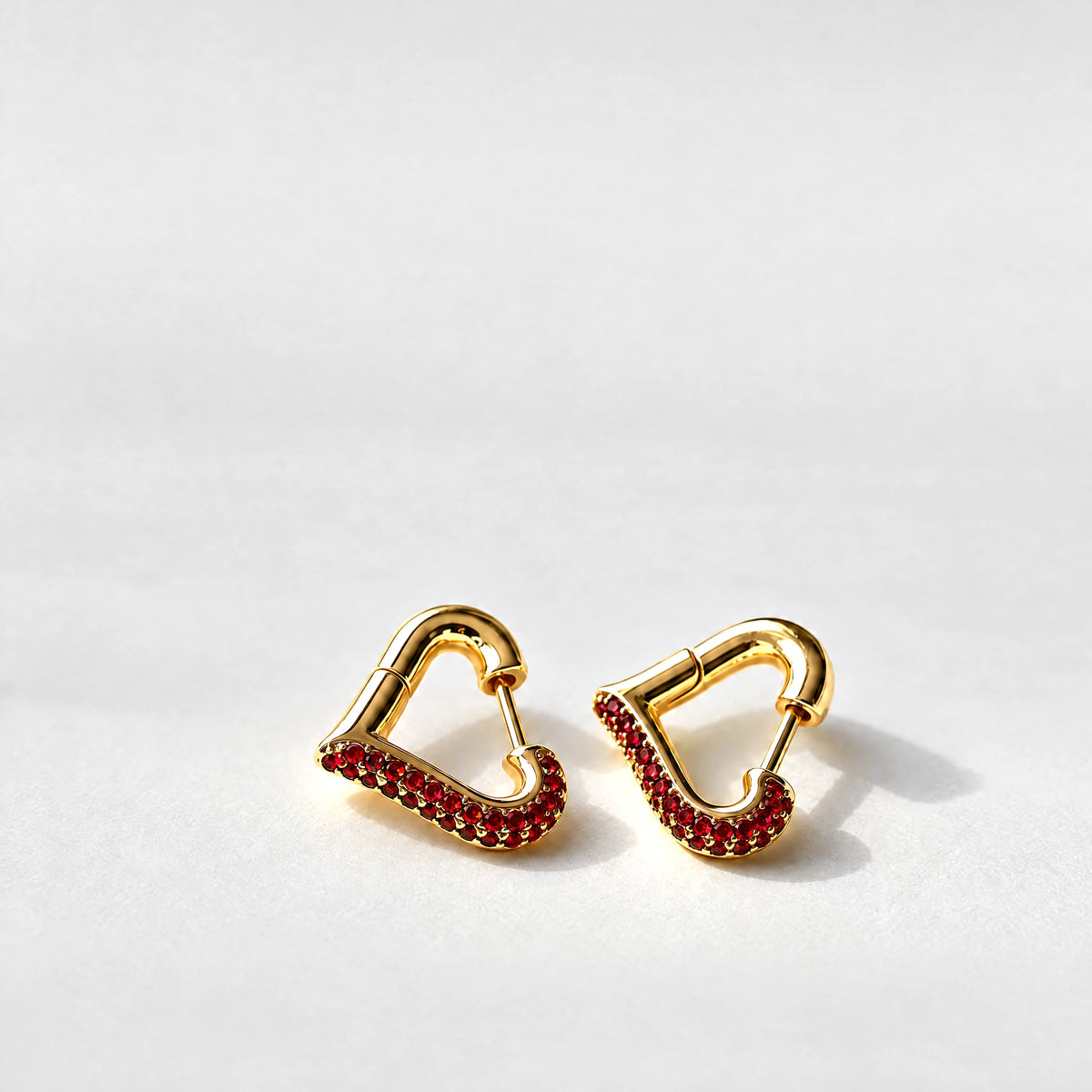 Gold Cora Crystal Heart Hoop Earrings with red crystals on a light grey background