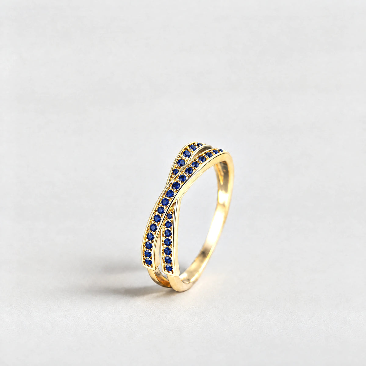 Gold Ivy Crossover Crystal Ring with blue crystals on a light grey background