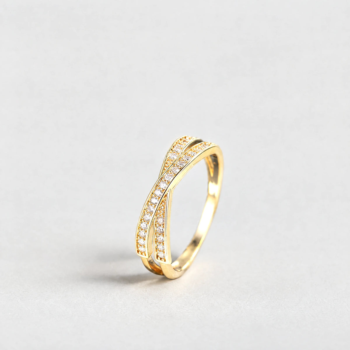 Gold Ivy Crossover Crystal Ring with clear crystals on a light grey background