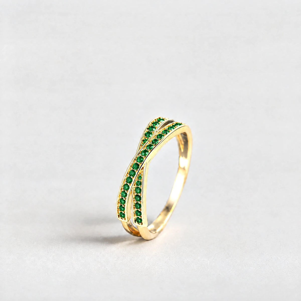 Gold Ivy Crossover Crystal Ring with green crystals on a light grey background