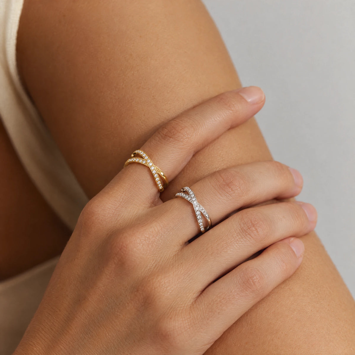 Hands crossed over a bare arm wearing the gold and the silver Ivy Crossover Crystal Ring