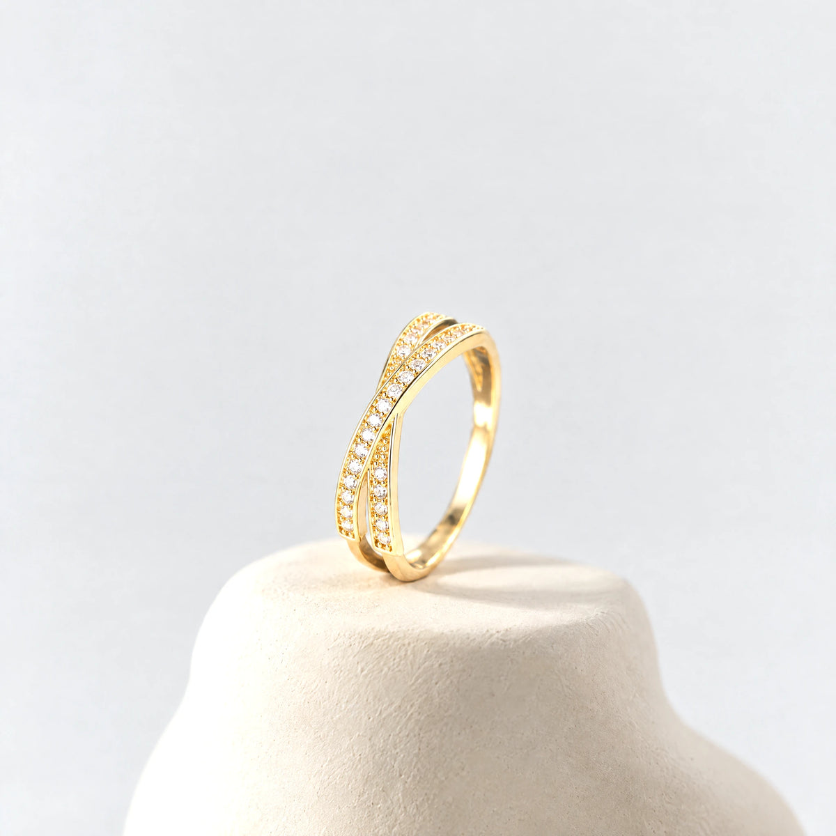 Gold Ivy Crossover Crystal Ring standing on a cream clay pedestal