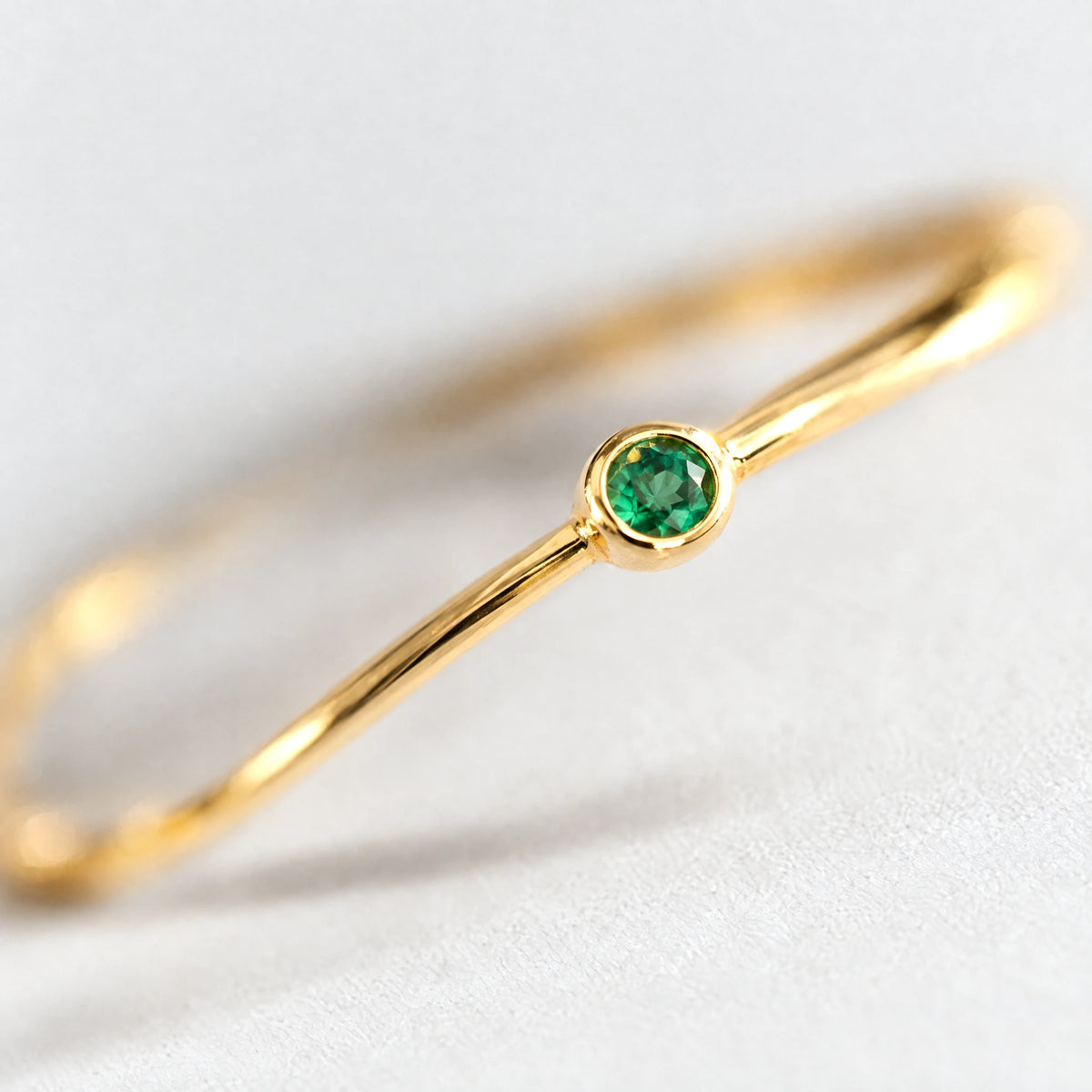 Close-up of the bezel-set emerald green stone on the gold Lena Birthstone Ring