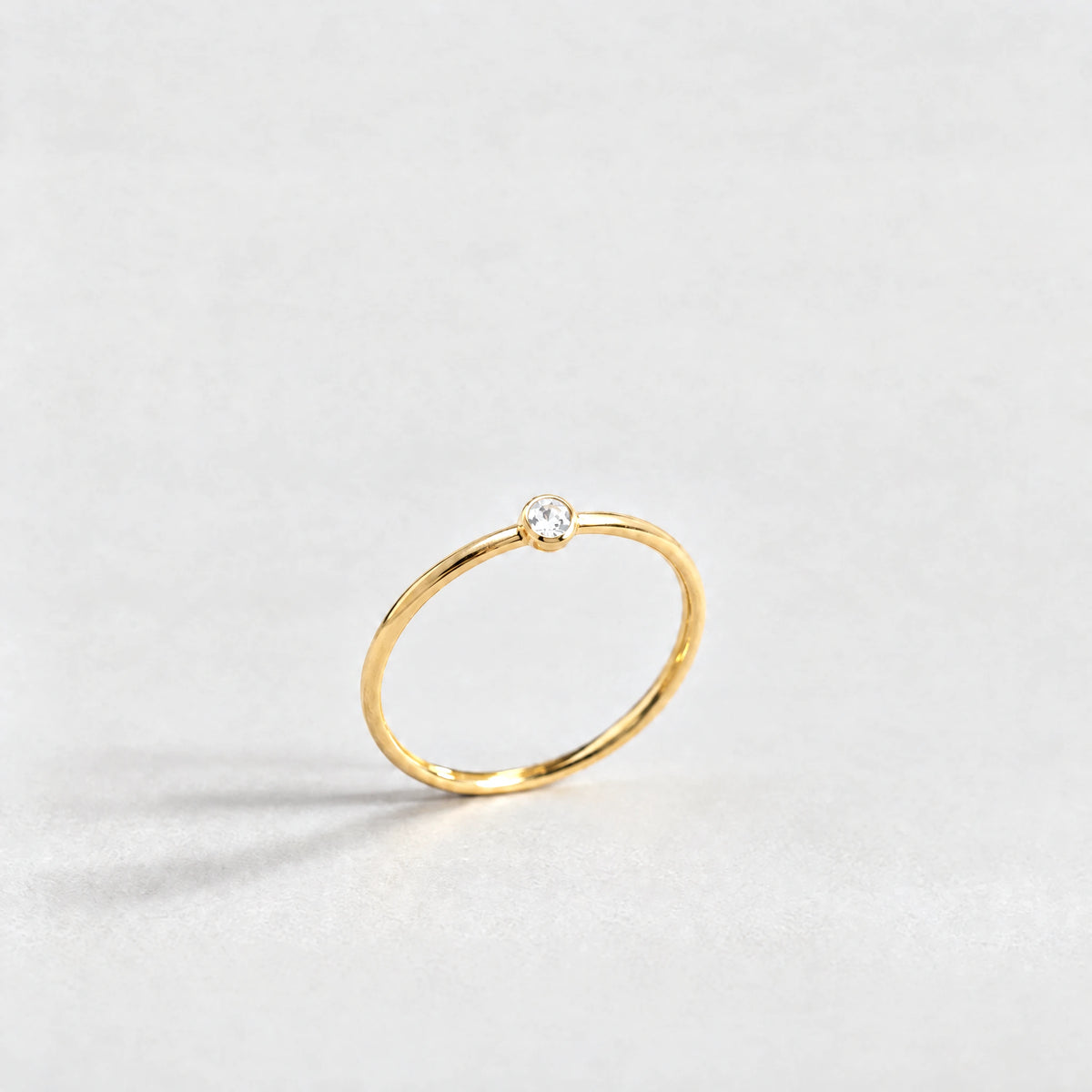 Gold Lena Birthstone Ring with crystal clear April birthstone-color crystal on a light grey background