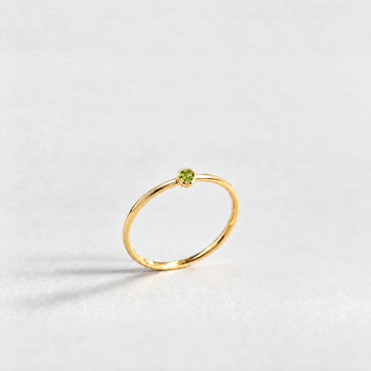 Gold Lena Birthstone Ring with peridot green August birthstone-color crystal on a light grey background