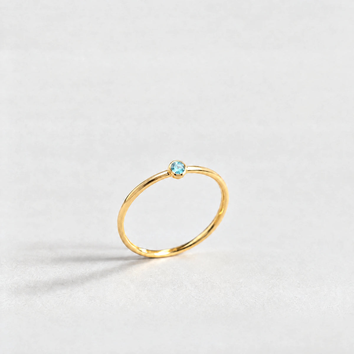Gold Lena Birthstone Ring with topaz blue December birthstone-color crystal on a light grey background