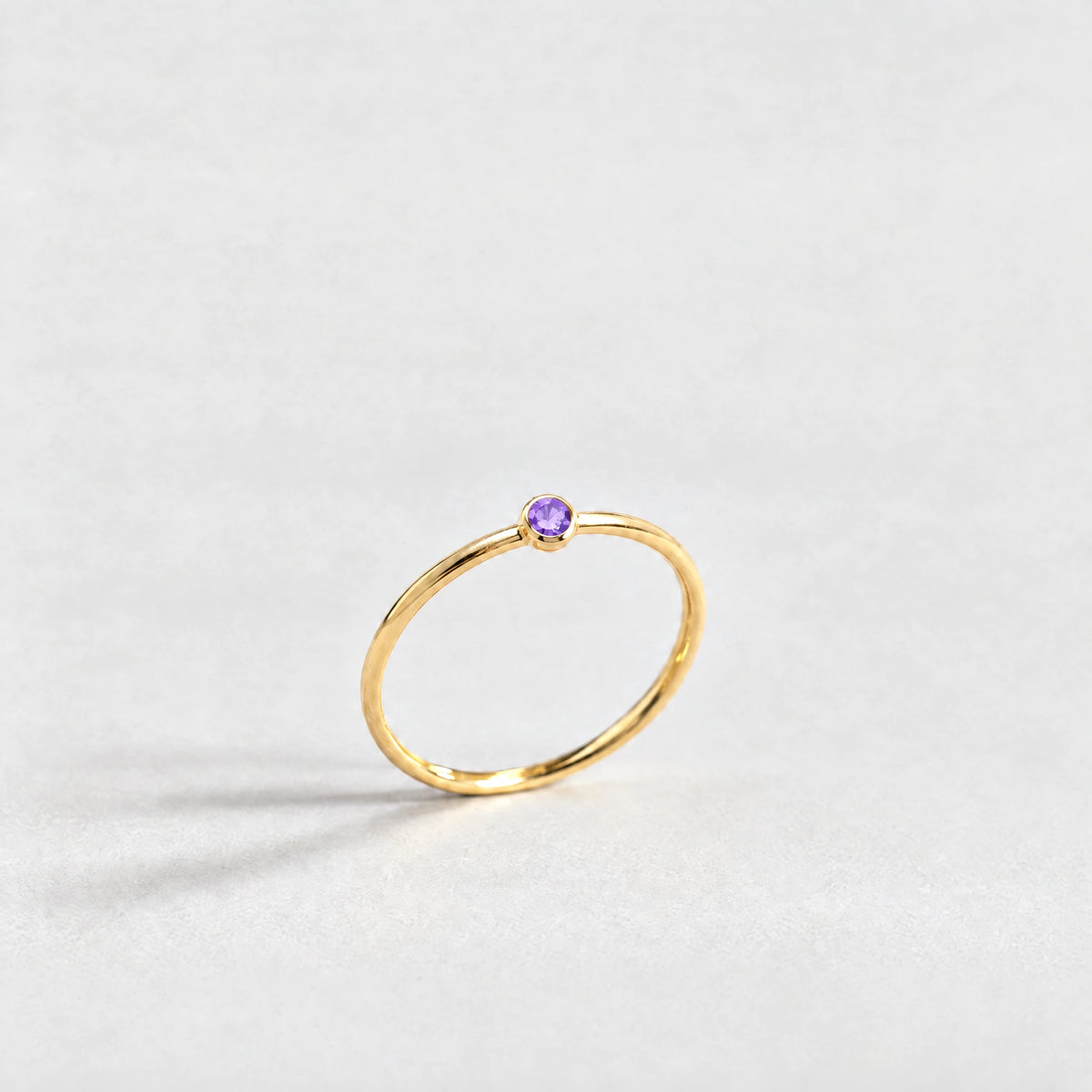 Gold Lena Birthstone Ring with amethyst violet February birthstone-color crystal on a light grey background