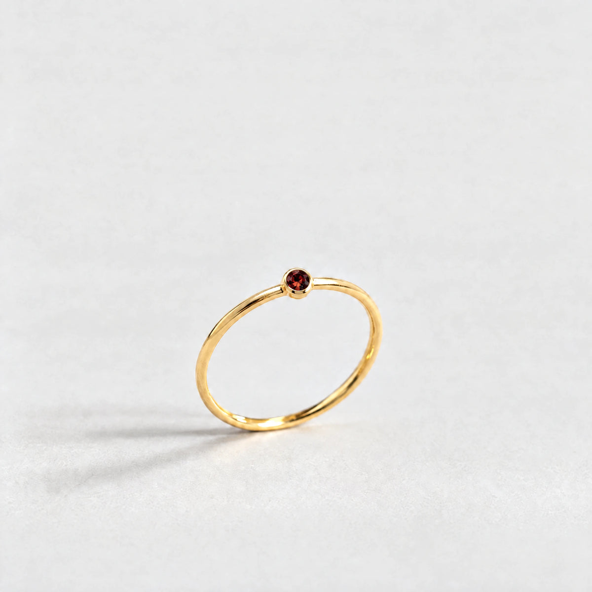 Gold Lena Birthstone Ring with garnet red January birthstone-color crystal on a light grey background