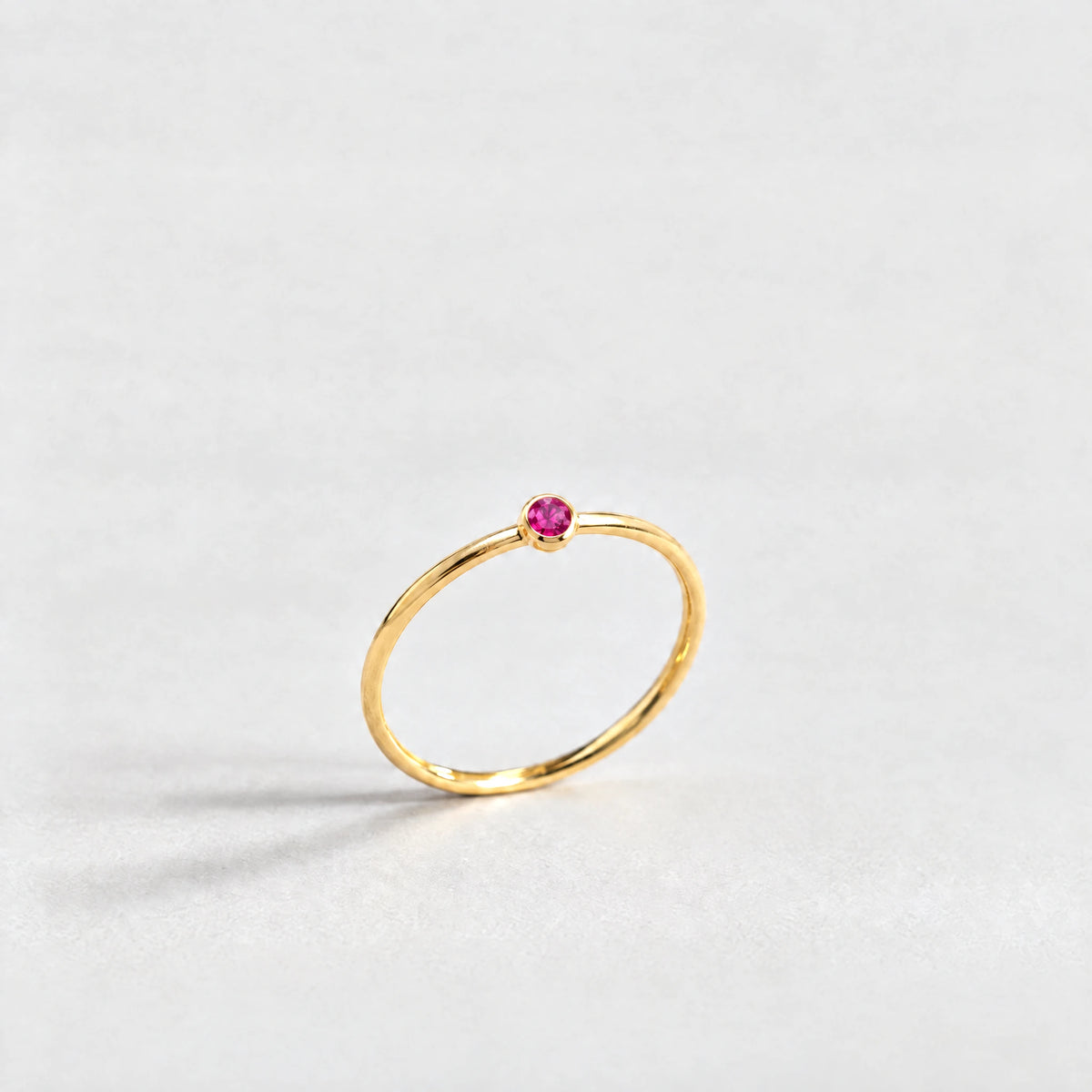 Gold Lena Birthstone Ring with ruby rose July birthstone-color crystal on a light grey background