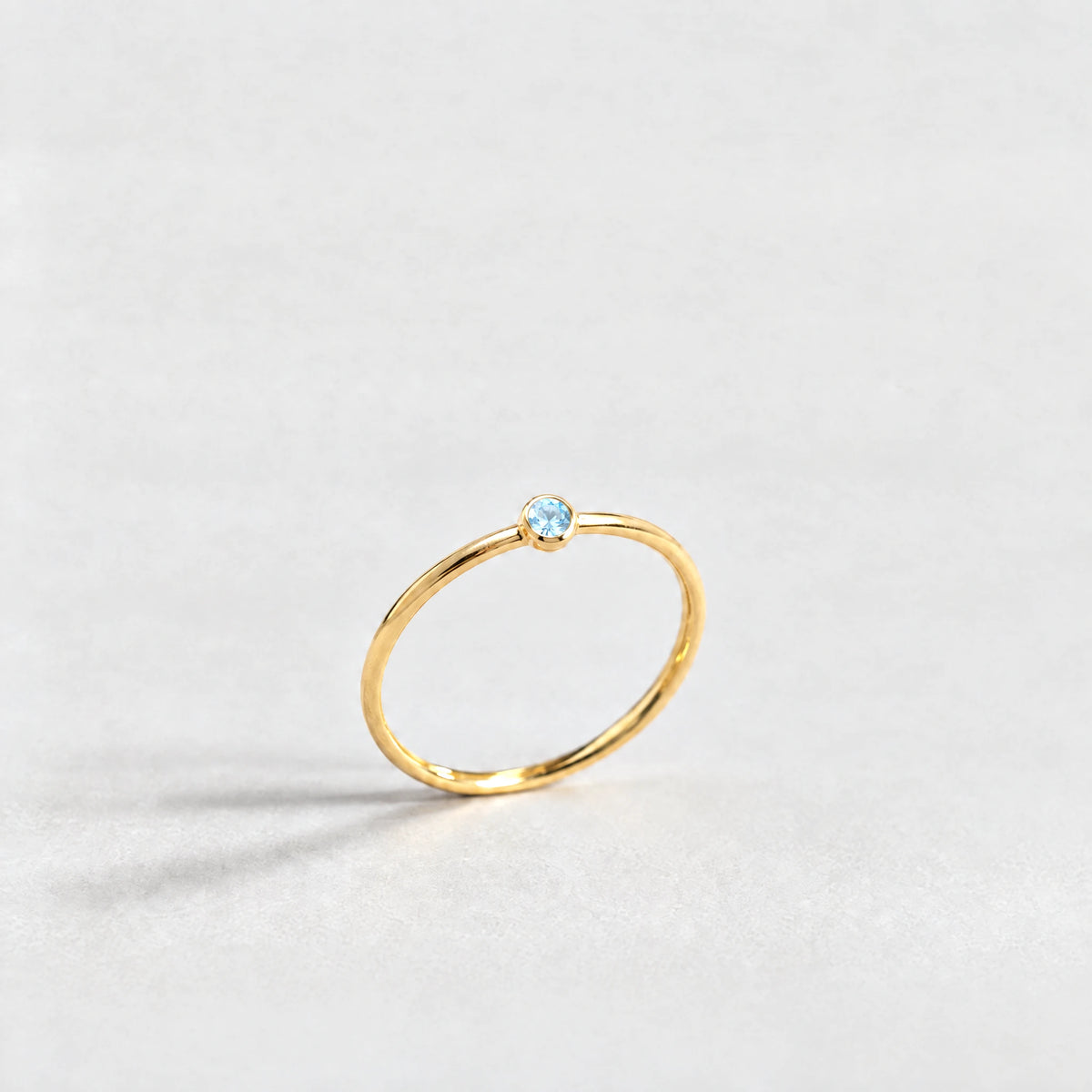 Gold Lena Birthstone Ring with aquamarine blue March birthstone-color crystal on a light grey background