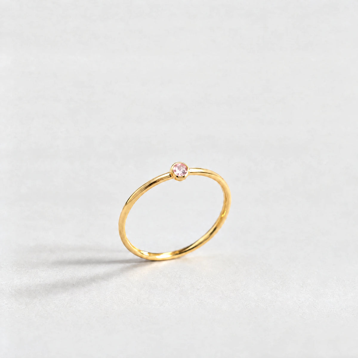 Gold Lena Birthstone Ring with tourmaline pink October birthstone-color crystal on a light grey background