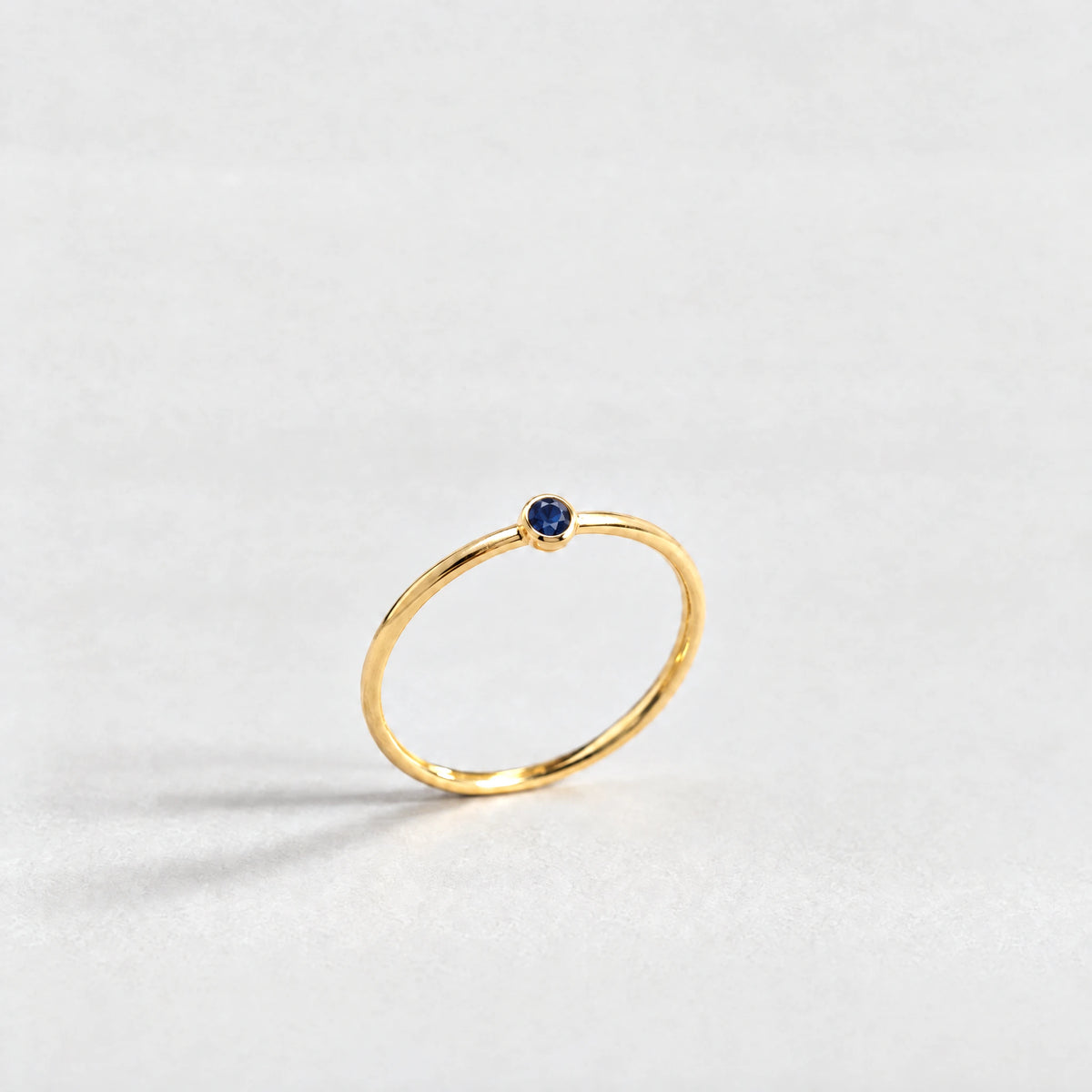 Gold Lena Birthstone Ring with sapphire blue September birthstone-color crystal on a light grey background
