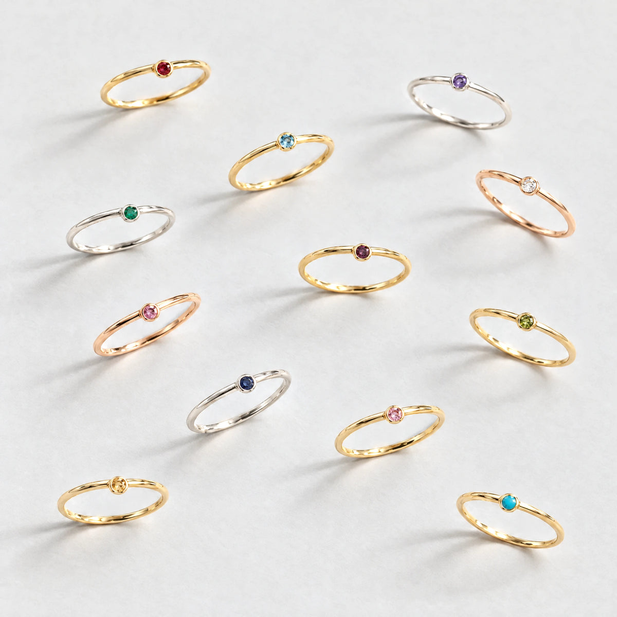 Twelve Lena Birthstone Rings in every birth month color on a light grey surface