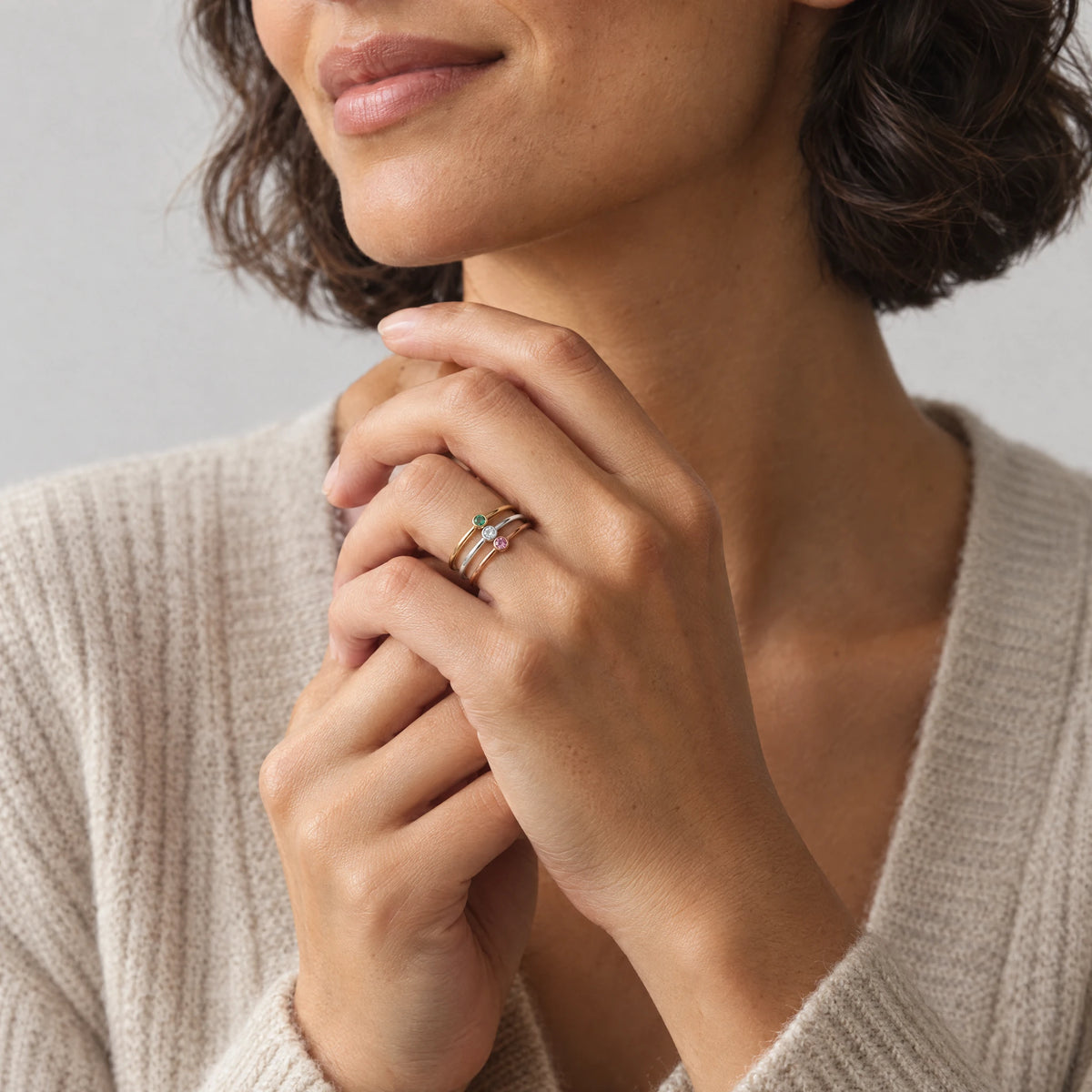 Woman with interlaced hands wearing three stacked Lena Birthstone Rings in green, clear and pink