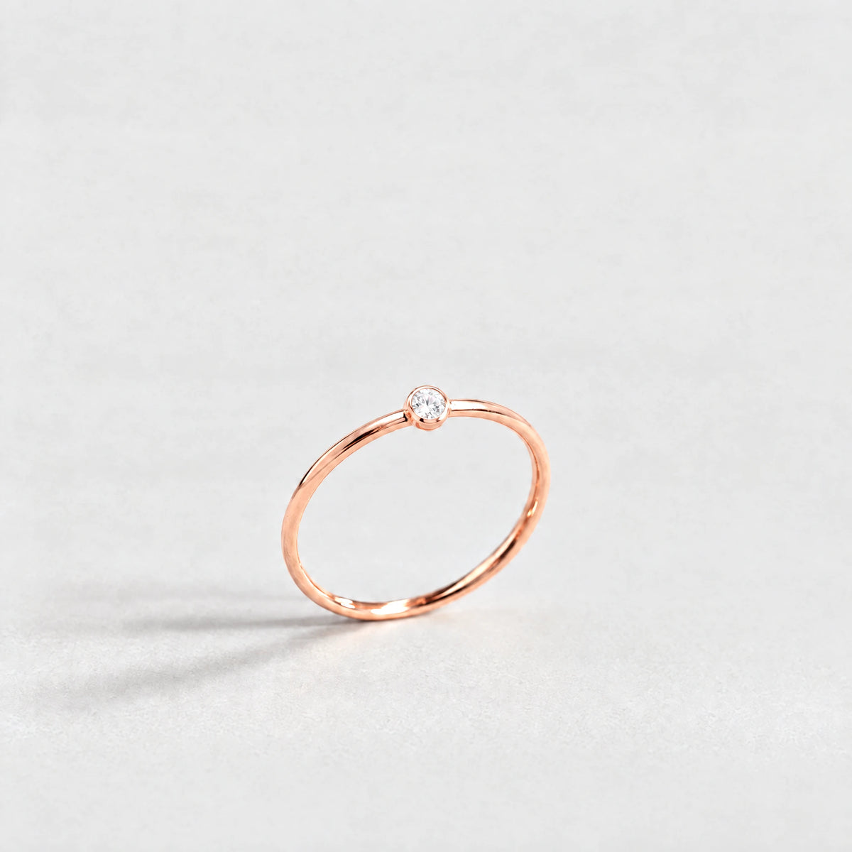 Rose gold Lena Birthstone Ring with crystal clear April birthstone-color crystal on a light grey background