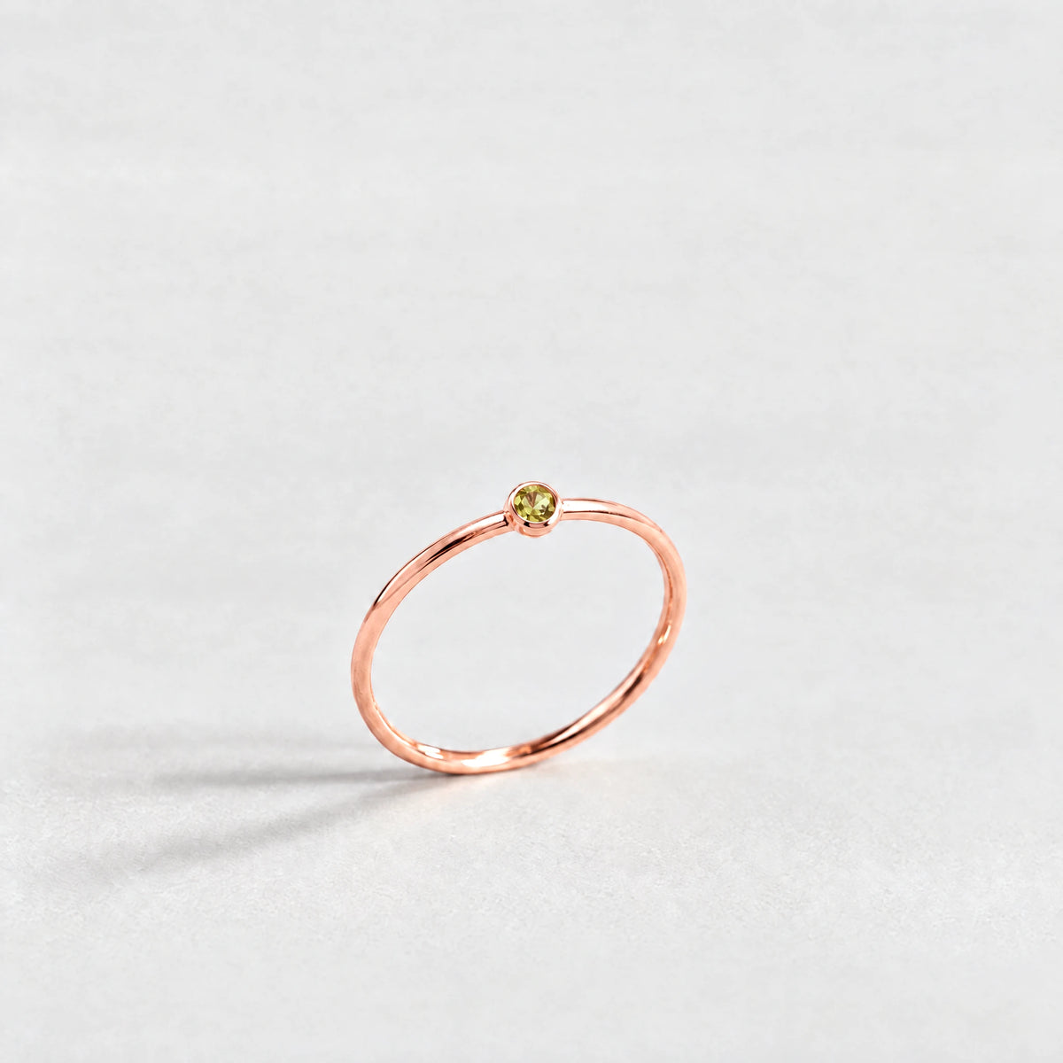 Rose gold Lena Birthstone Ring with peridot green August birthstone-color crystal on a light grey background