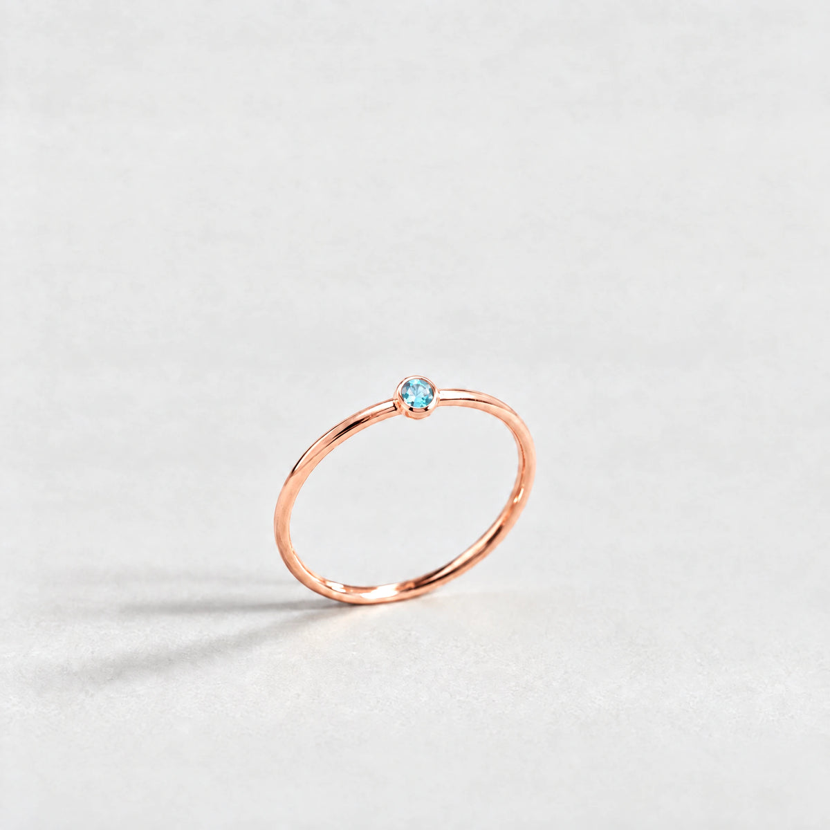 Rose gold Lena Birthstone Ring with topaz blue December birthstone-color crystal on a light grey background