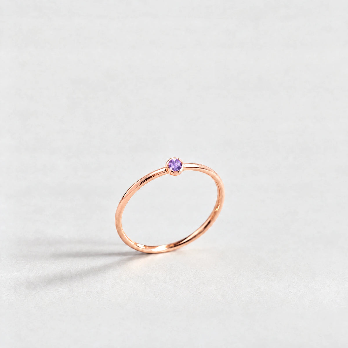 Rose gold Lena Birthstone Ring with amethyst violet February birthstone-color crystal on a light grey background