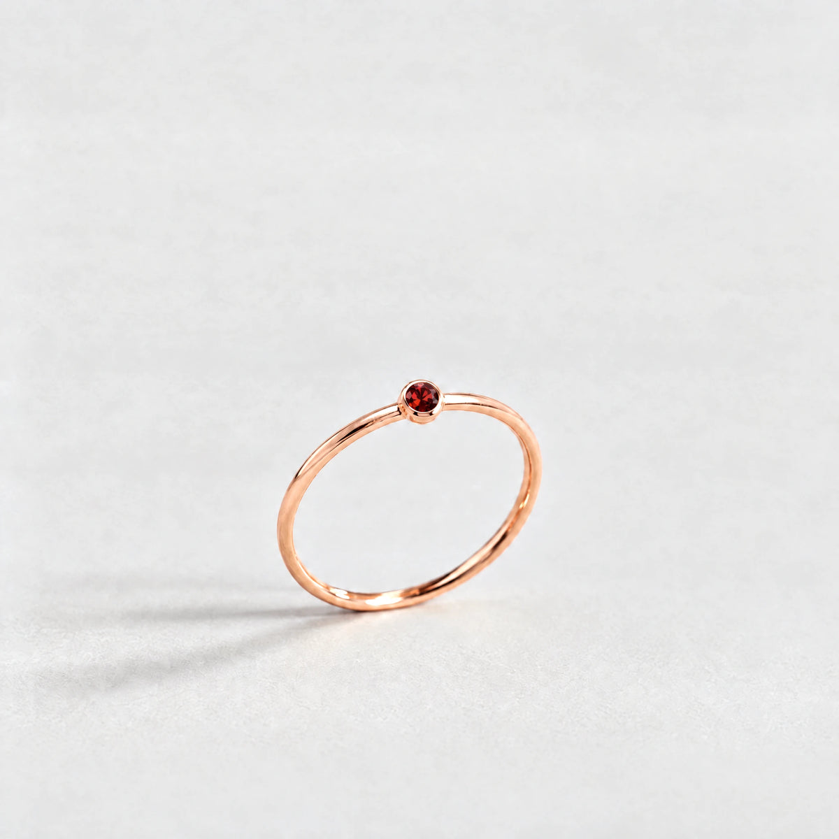 Rose gold Lena Birthstone Ring with garnet red January birthstone-color crystal on a light grey background