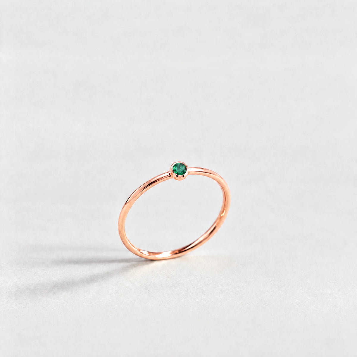 Rose gold Lena Birthstone Ring with emerald green May birthstone-color crystal on a light grey background