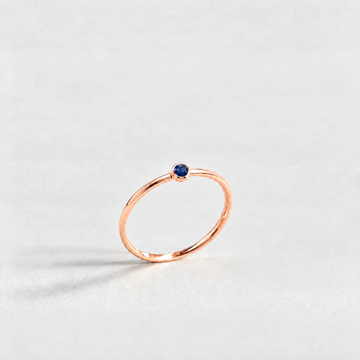 Rose gold Lena Birthstone Ring with sapphire blue September birthstone-color crystal on a light grey background