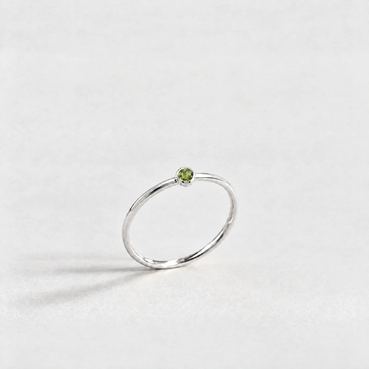 Silver Lena Birthstone Ring with peridot green August birthstone-color crystal on a light grey background