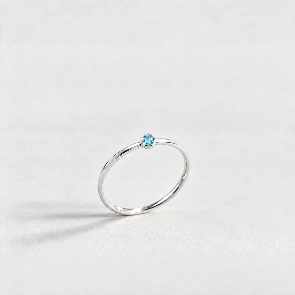 Silver Lena Birthstone Ring with topaz blue December birthstone-color crystal on a light grey background