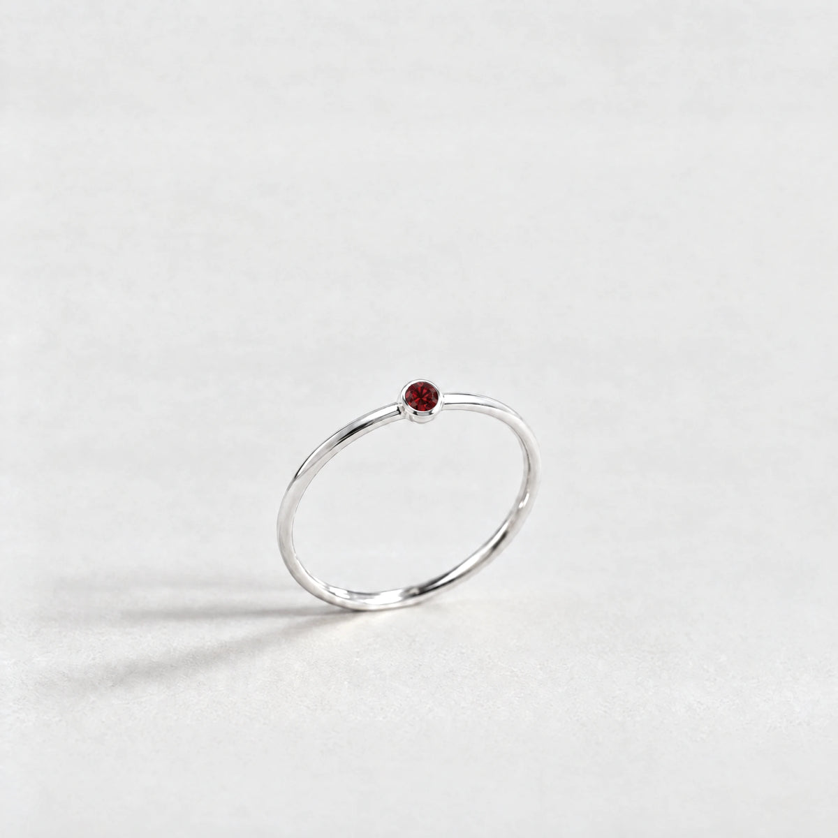 Silver Lena Birthstone Ring with garnet red January birthstone-color crystal on a light grey background