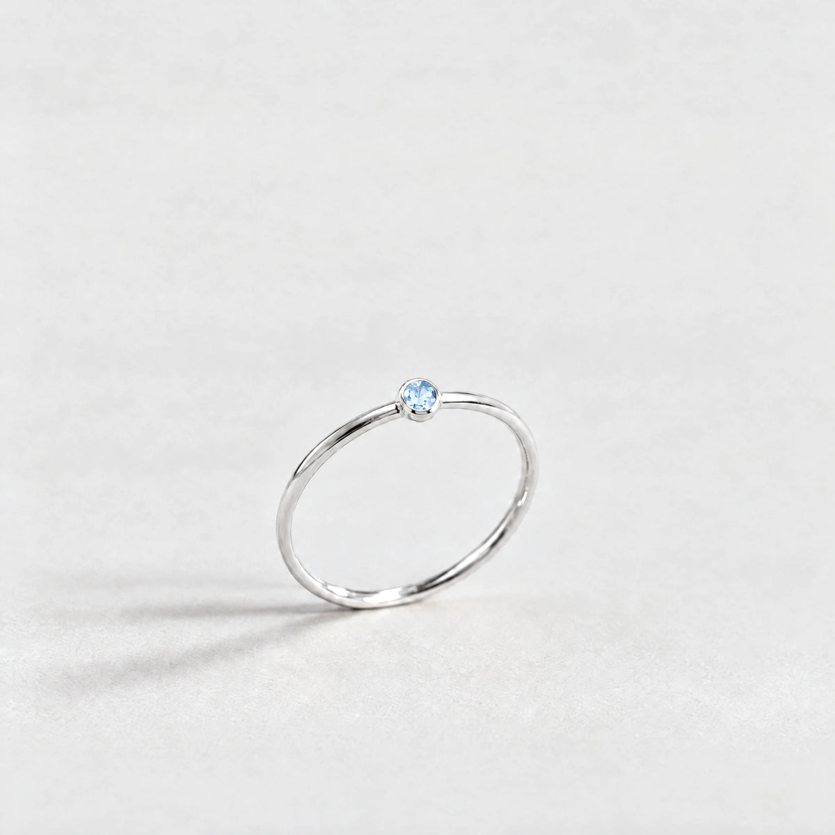 Silver Lena Birthstone Ring with aquamarine blue March birthstone-color crystal on a light grey background