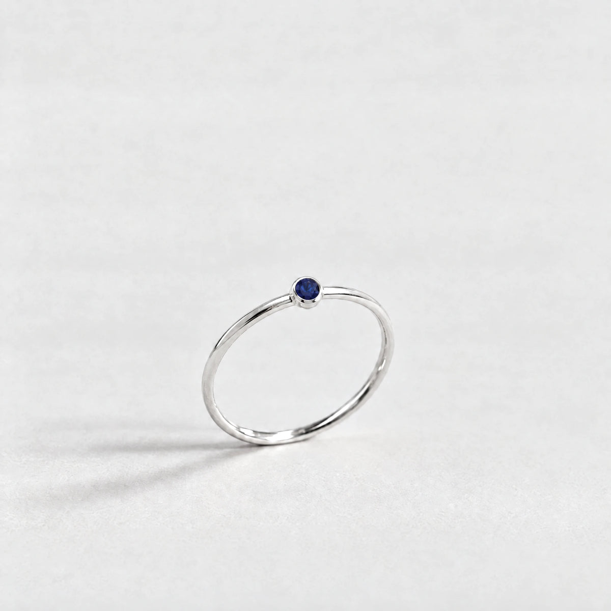 Silver Lena Birthstone Ring with sapphire blue September birthstone-color crystal on a light grey background