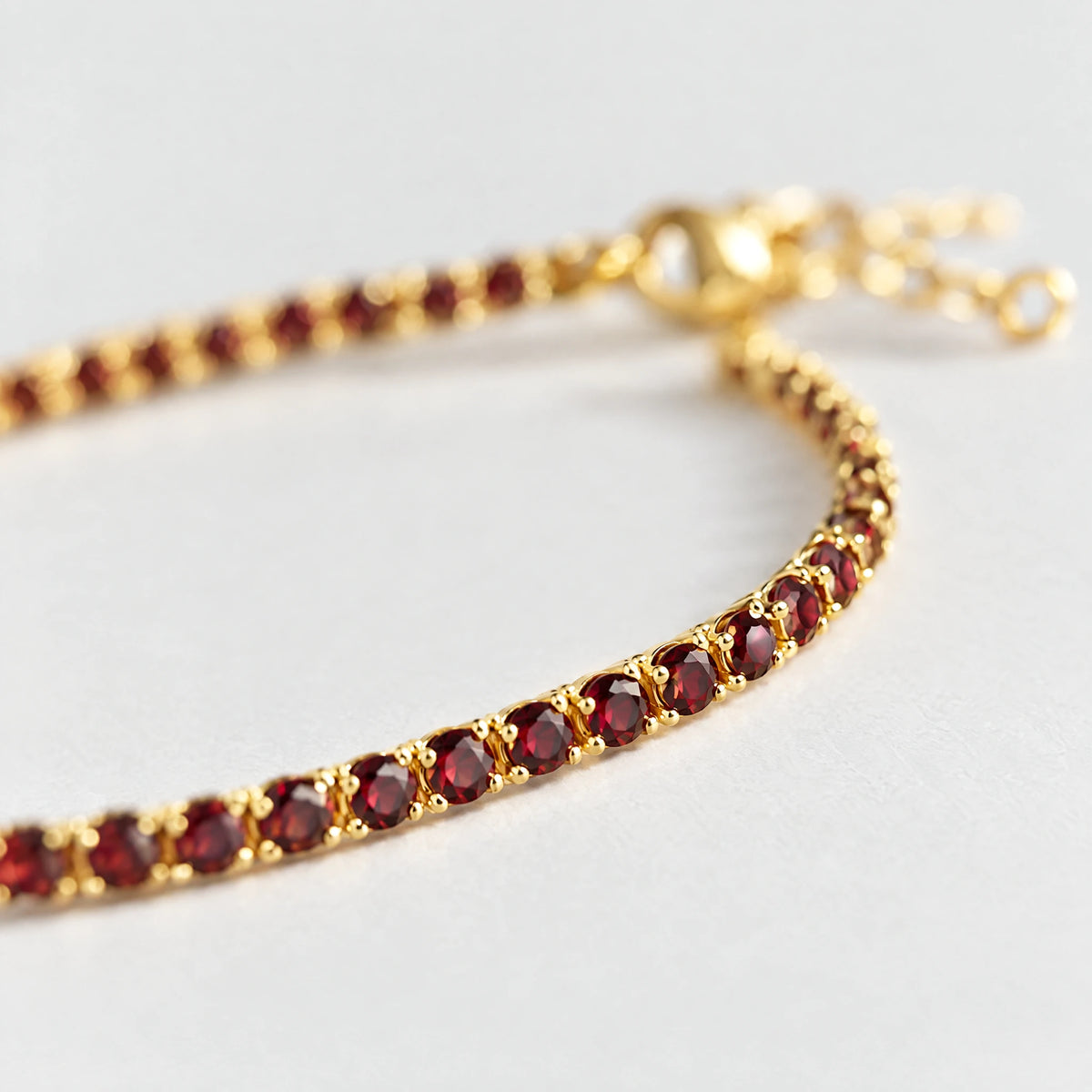 Close-up of the prong-set garnet-red crystals on the gold MAYA Birthstone Tennis Bracelet