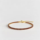MAYA Birthstone Tennis Bracelet in gold plating with a single row of garnet-red crystals on a light grey background