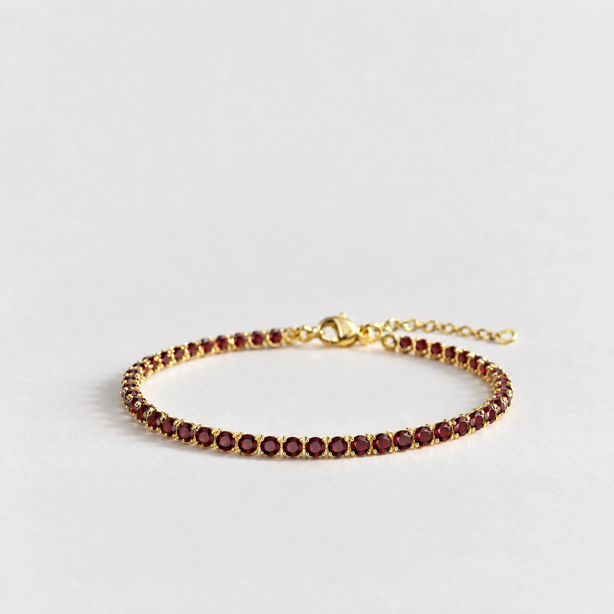 MAYA Birthstone Tennis Bracelet in gold plating with a single row of garnet-red crystals on a light grey background