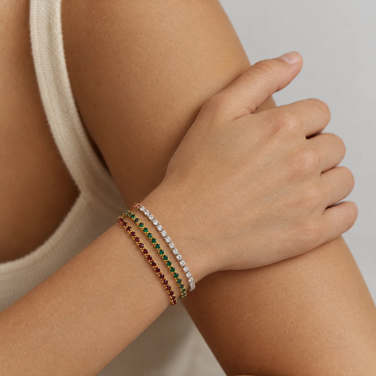 Woman's wrist wearing a stack of three MAYA Birthstone Tennis Bracelets in garnet red, emerald green and clear crystals