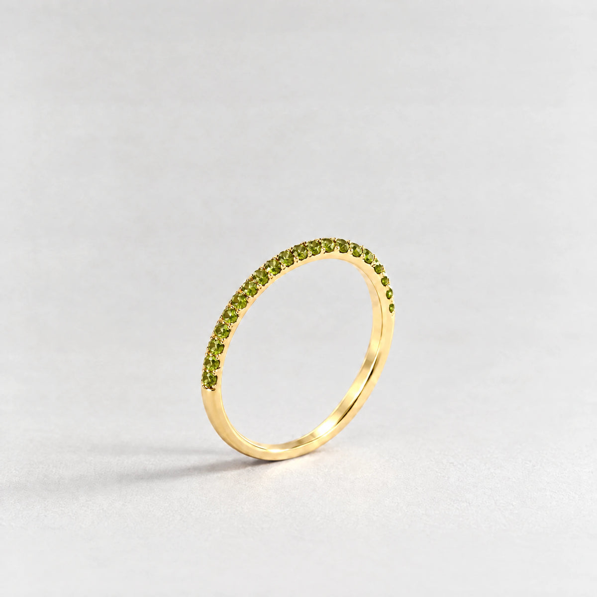 Gold Nora Birthstone Stacking Ring with peridot green August birthstone-color crystals on a light grey background