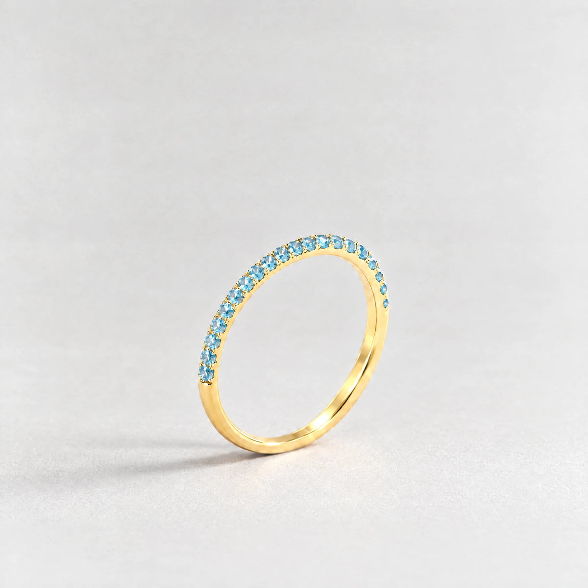 Gold Nora Birthstone Stacking Ring with topaz blue December birthstone-color crystals on a light grey background