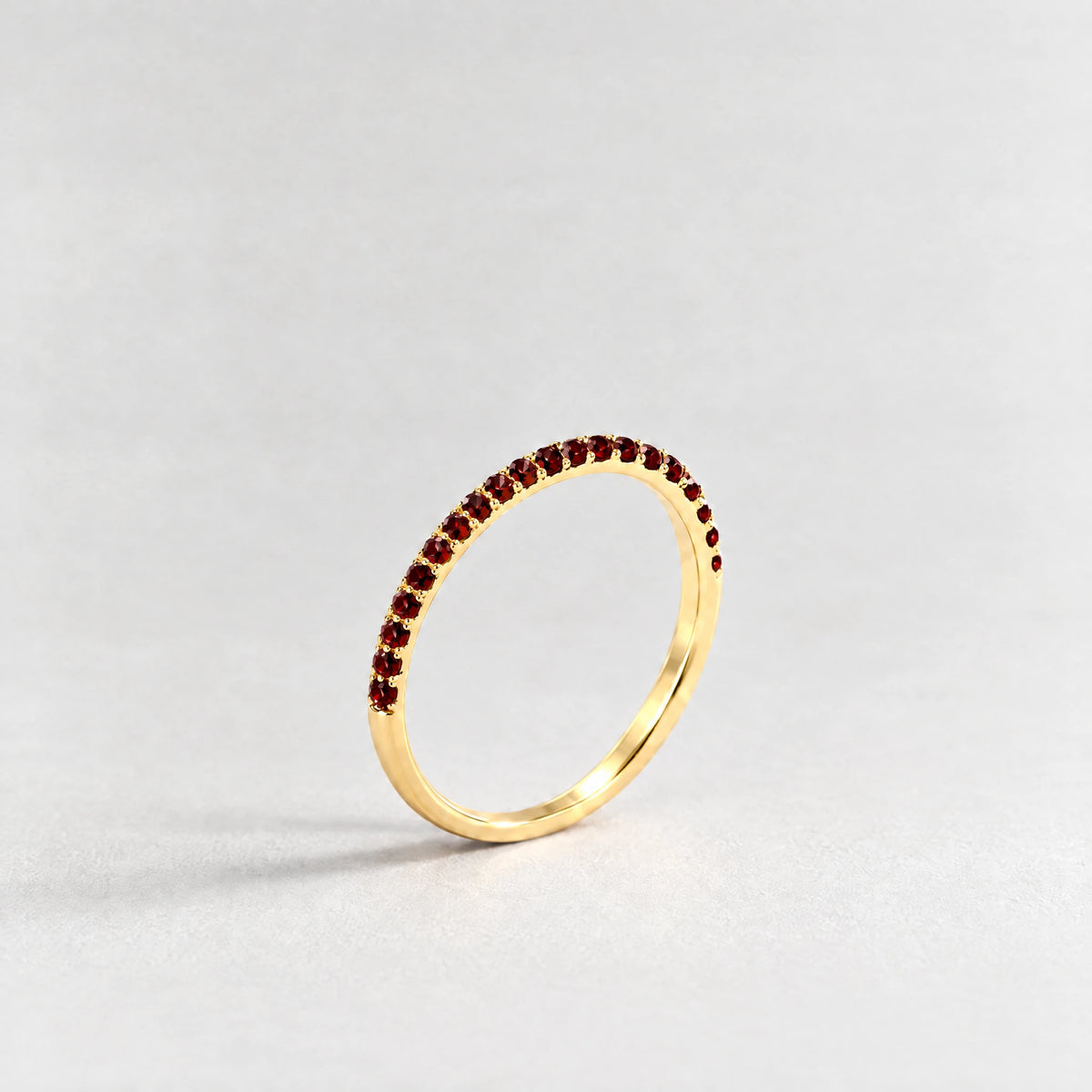 Gold Nora Birthstone Stacking Ring with garnet red January birthstone-color crystals on a light grey background