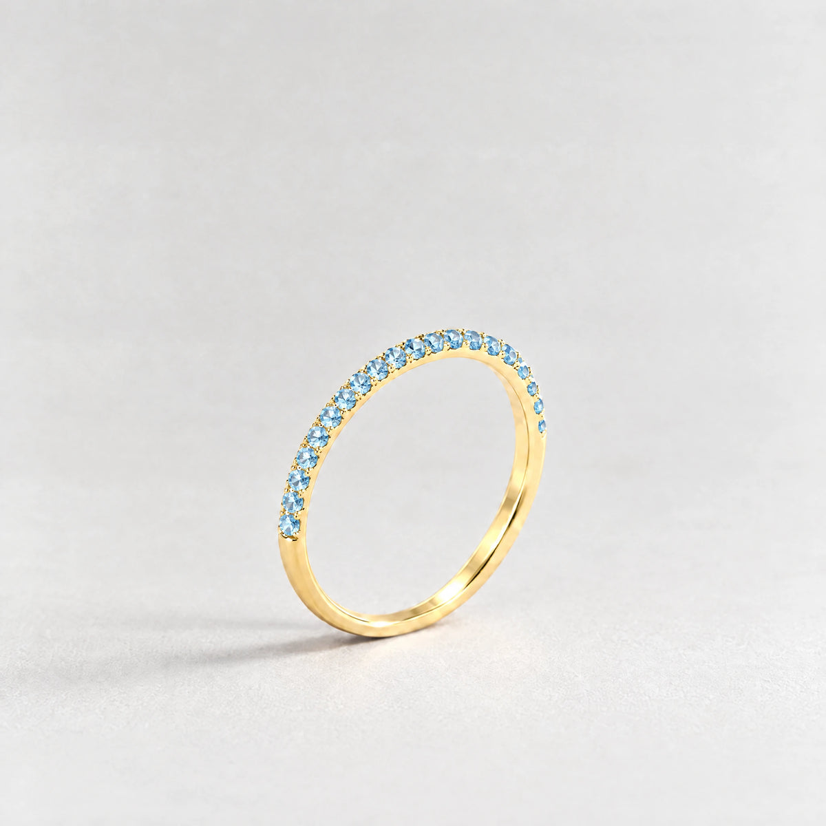 Gold Nora Birthstone Stacking Ring with aquamarine blue March birthstone-color crystals on a light grey background
