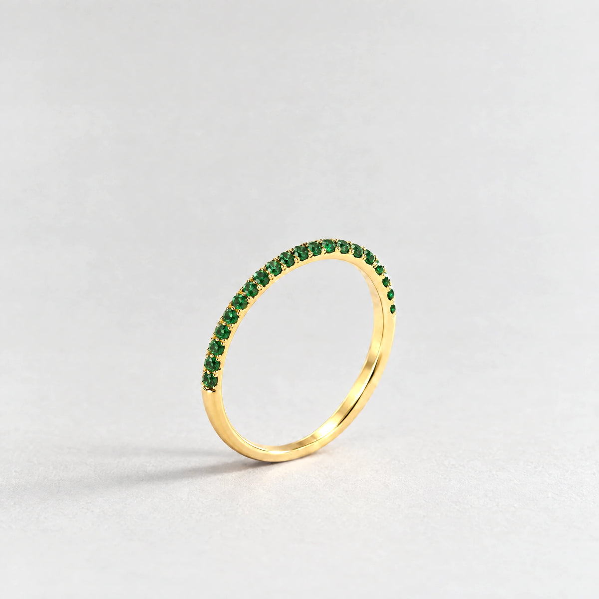 Gold Nora Birthstone Stacking Ring with emerald green May birthstone-color crystals on a light grey background