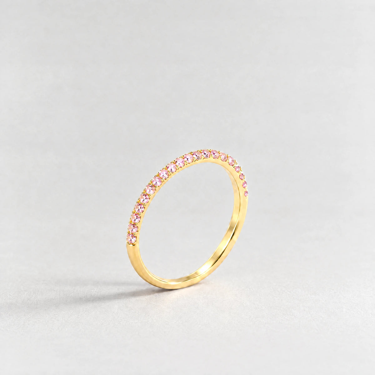 Gold Nora Birthstone Stacking Ring with tourmaline pink October birthstone-color crystals on a light grey background