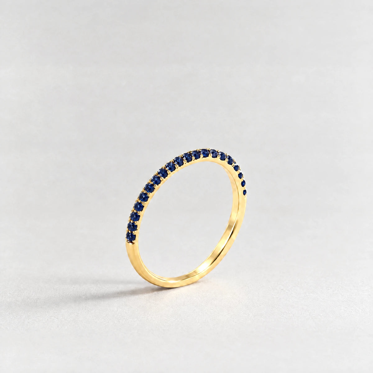 Gold Nora Birthstone Stacking Ring with sapphire blue September birthstone-color crystals on a light grey background