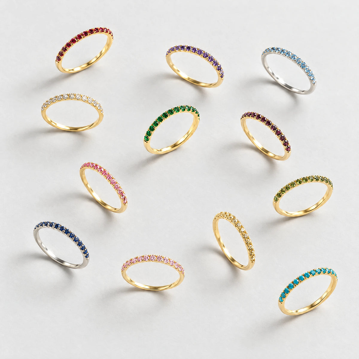 Twelve Nora Birthstone Stacking Rings in every birth month color on a light grey surface